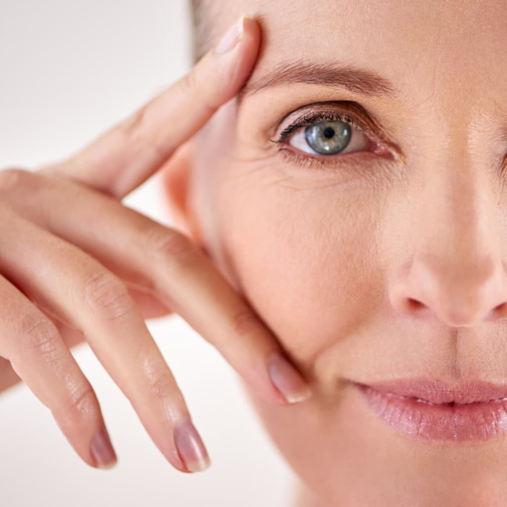 Mature woman gently touching the eye and temple area during a calm daily face care ritual